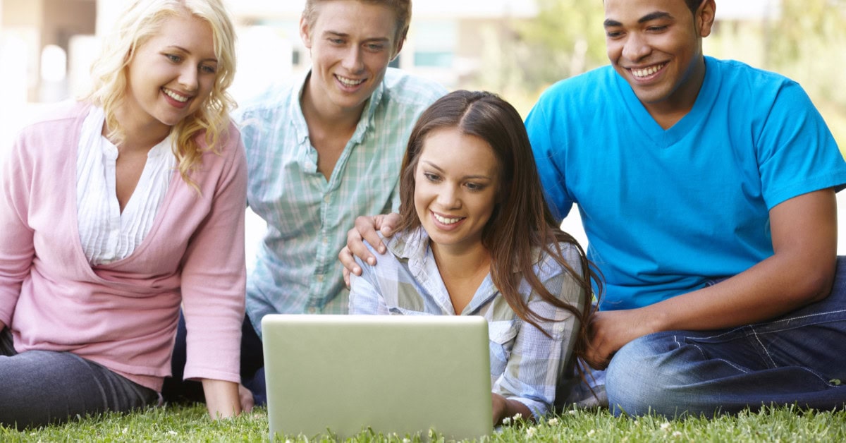 college students sitting on lawn surrounding laptop - budget laptops for students