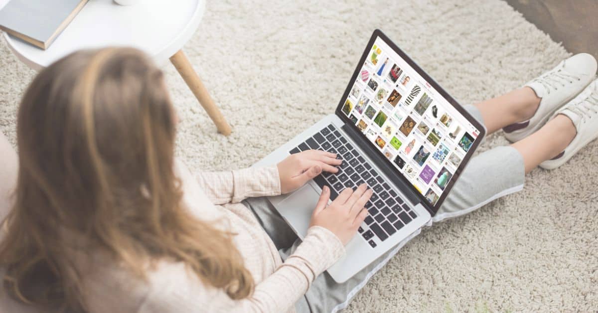 top down view of woman working on laptop sitting on floor with pinterest website on computer screen.