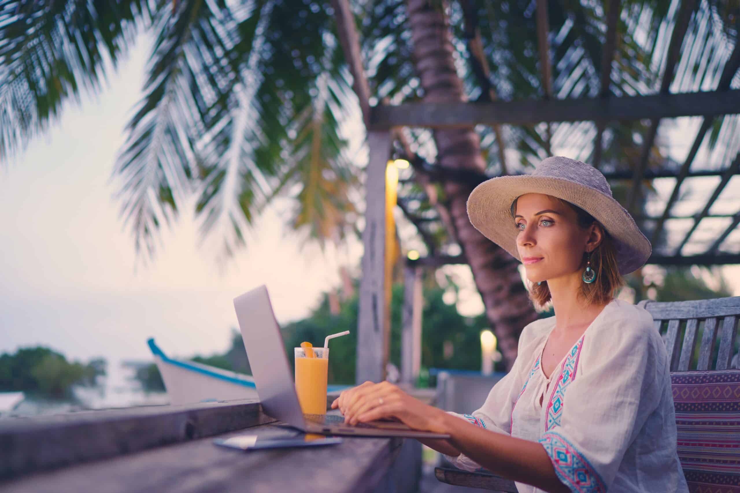 Pretty young woman using laptop in cafe on tropical beach