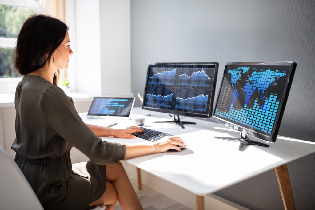 Young female stock market broker analyzing graph on computer at workplace